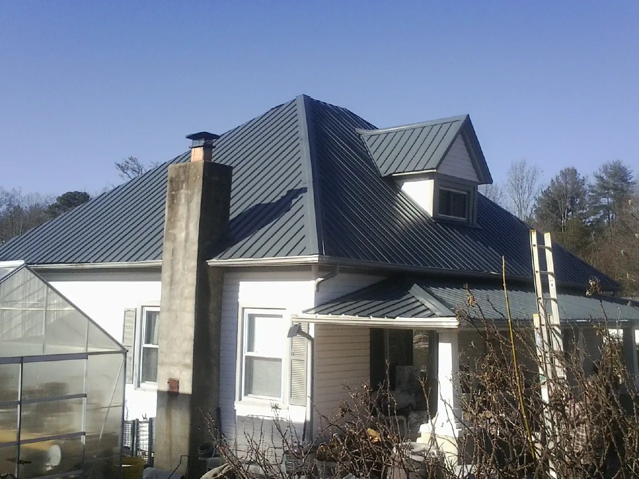 Dark blue standing seam metal roof on a white farmhouse with dormer — Slate & Tile Roof Repair by Roofing Brothers in Fort Dodge
