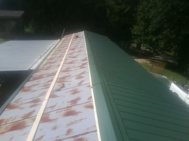 Old rusted panels beside newly installed green metal roofing — Wind Damage Roof Repair by Roofing Brothers in Fort Dodge