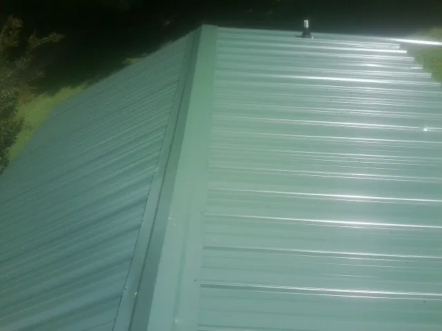 New green metal panels meeting at the ridge of a roof — Flat Roof Repair work by our crew in Fort Dodge