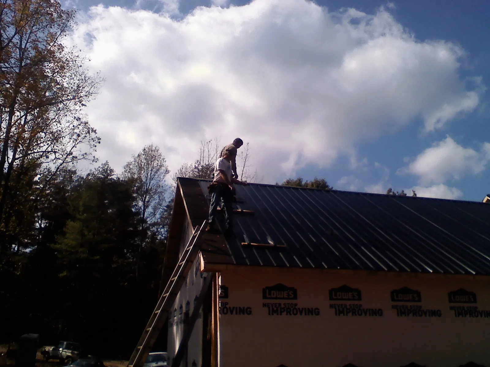 Roofer fastening dark metal panels high against a cloudy sky, from a Roof Inspection job in Fort Dodge