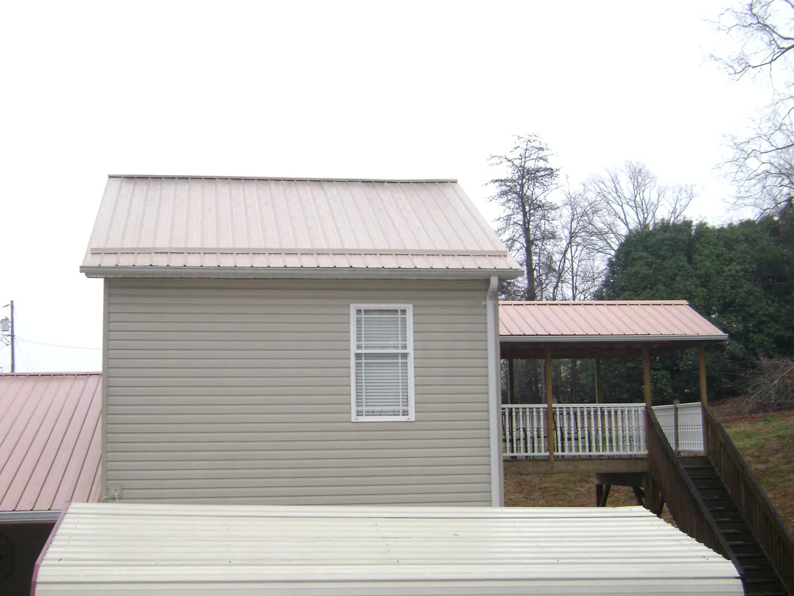Tan metal roofs on a two story addition and attached porch, from a Roof Replacement job in Fort Dodge