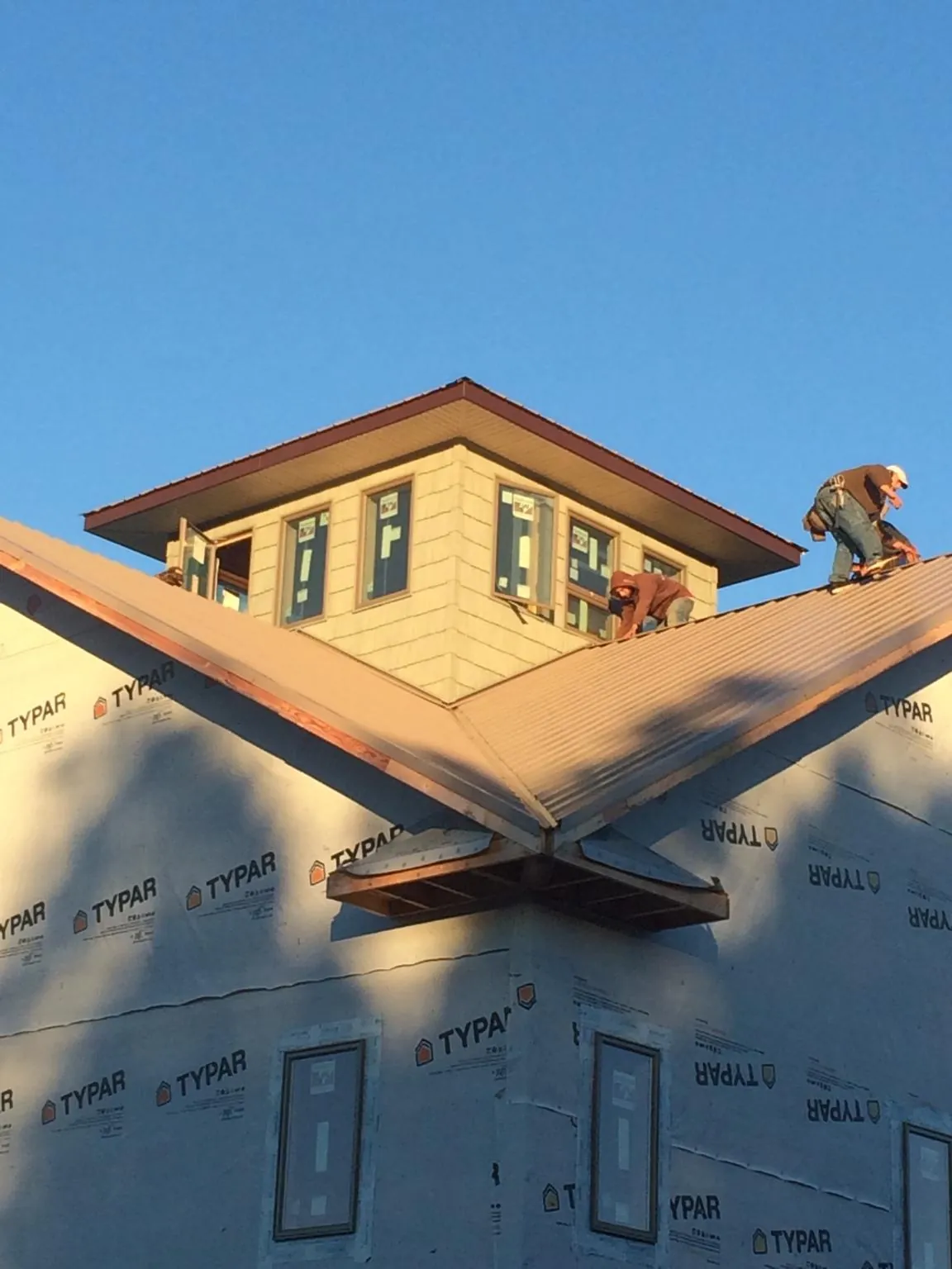 Roofers working around a rooftop cupola on a new metal roof at sunset — Roof Waterproofing in Fort Dodge by Roofing Brothers